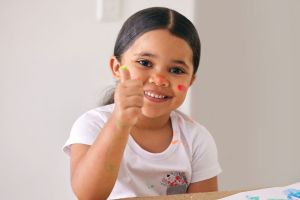 Young girl fingerpainting with thumbs up